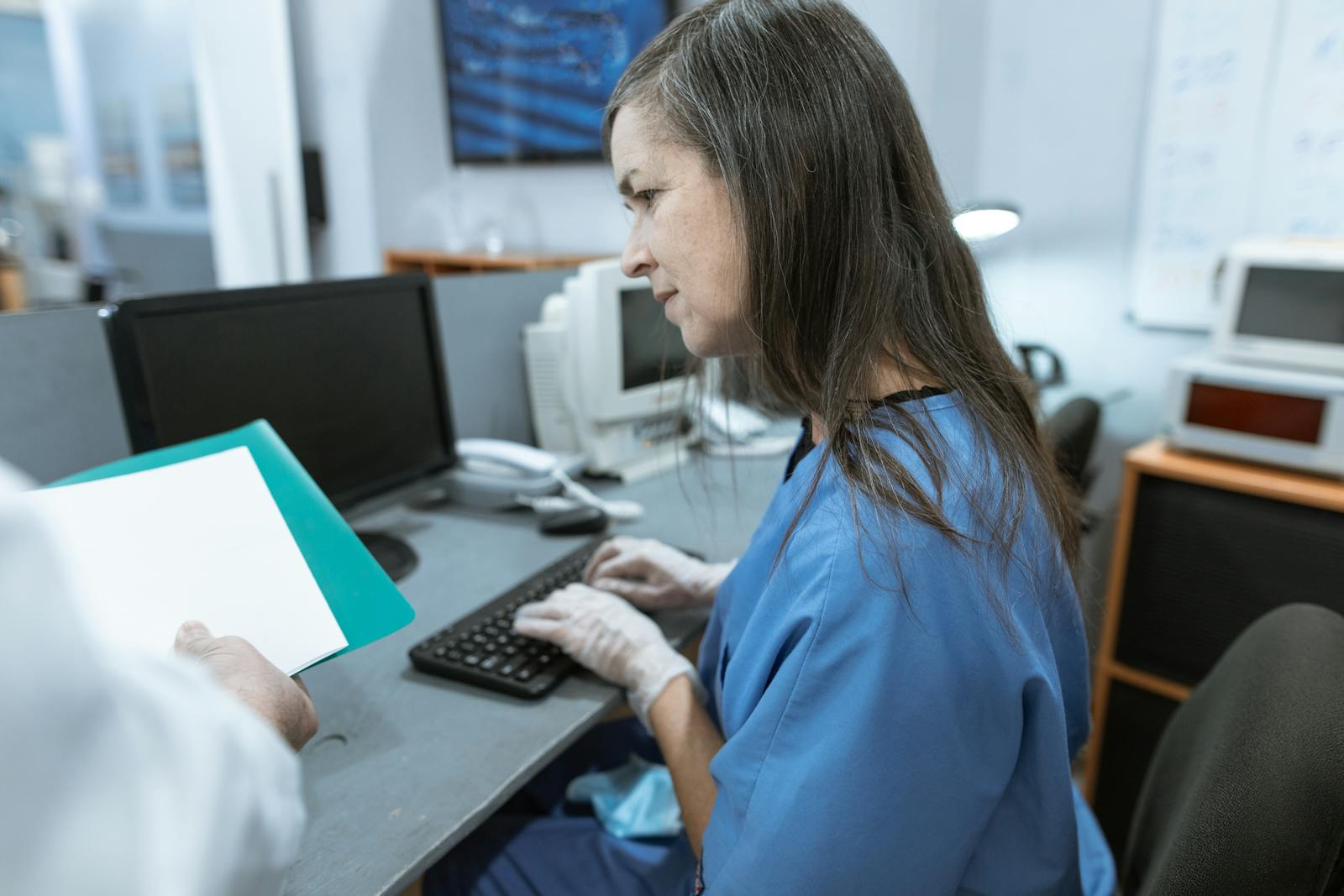 Photo by RDNE Stock project Nurse in scrubs typing on a keyboard at a medical workstation.