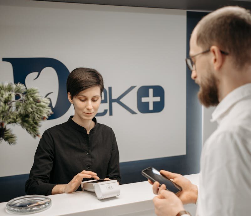 Customer making a cashless payment at a clinic reception using a smartphone and a wireless terminal.