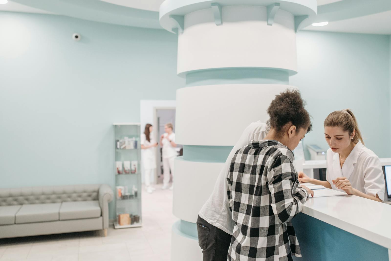 Photo by Pavel Danilyuk Healthcare professionals assisting at a modern clinic reception desk.